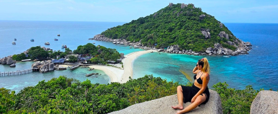 Tropical island beach view with a woman sitting on a rock